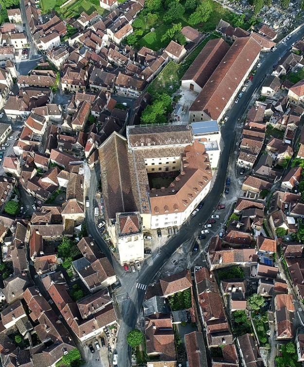 Vue aérienne d’un centre historique aux toits de tuiles rouges, autour d’un bâtiment patrimonial et de ruelles anciennes